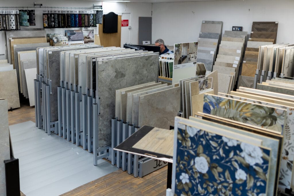 Rows of large porcelain tile boards on display racks in the Miller Wholesale tile showroom, with floral patterned samples in the foreground