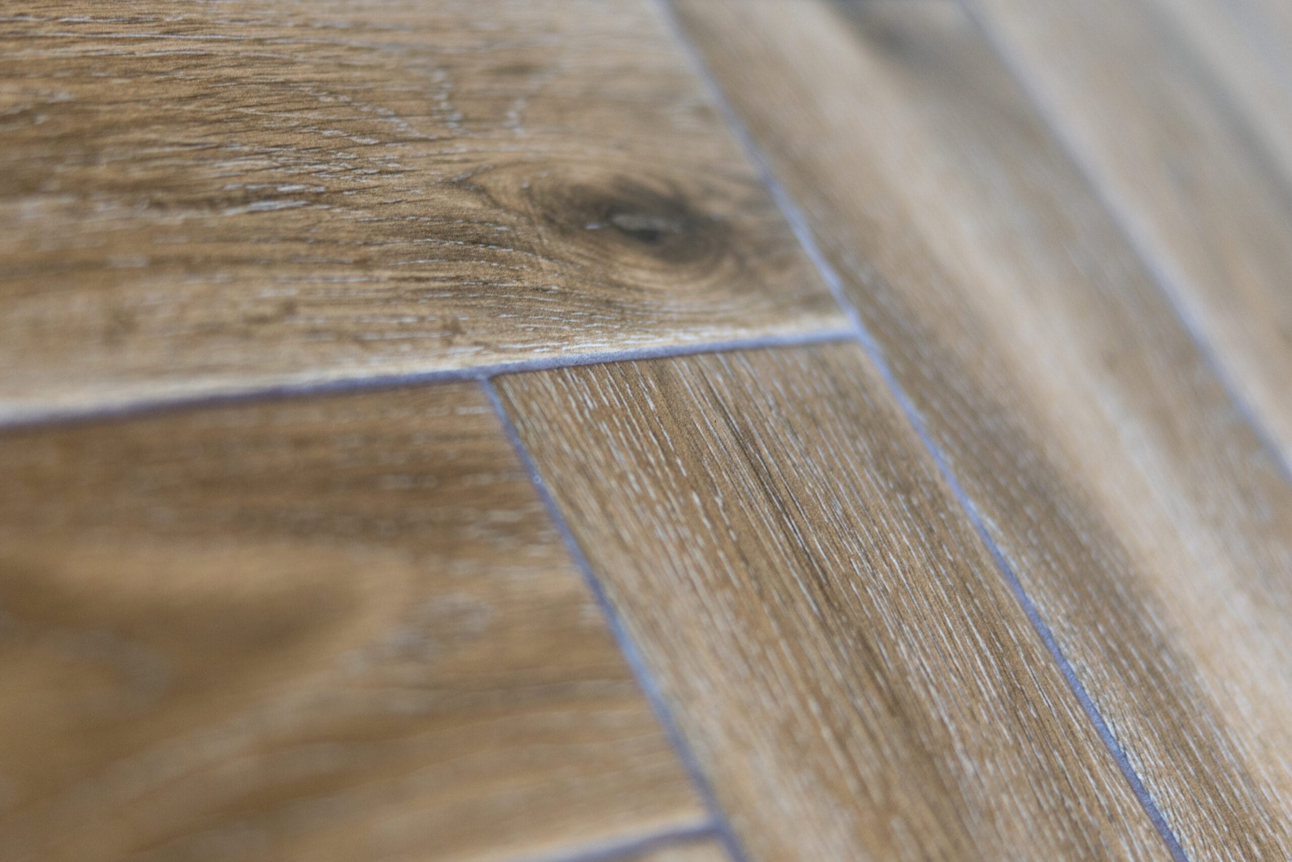 Close-up of textured wood-effect porcelain floor tiles laid in herringbone with grey grout lines