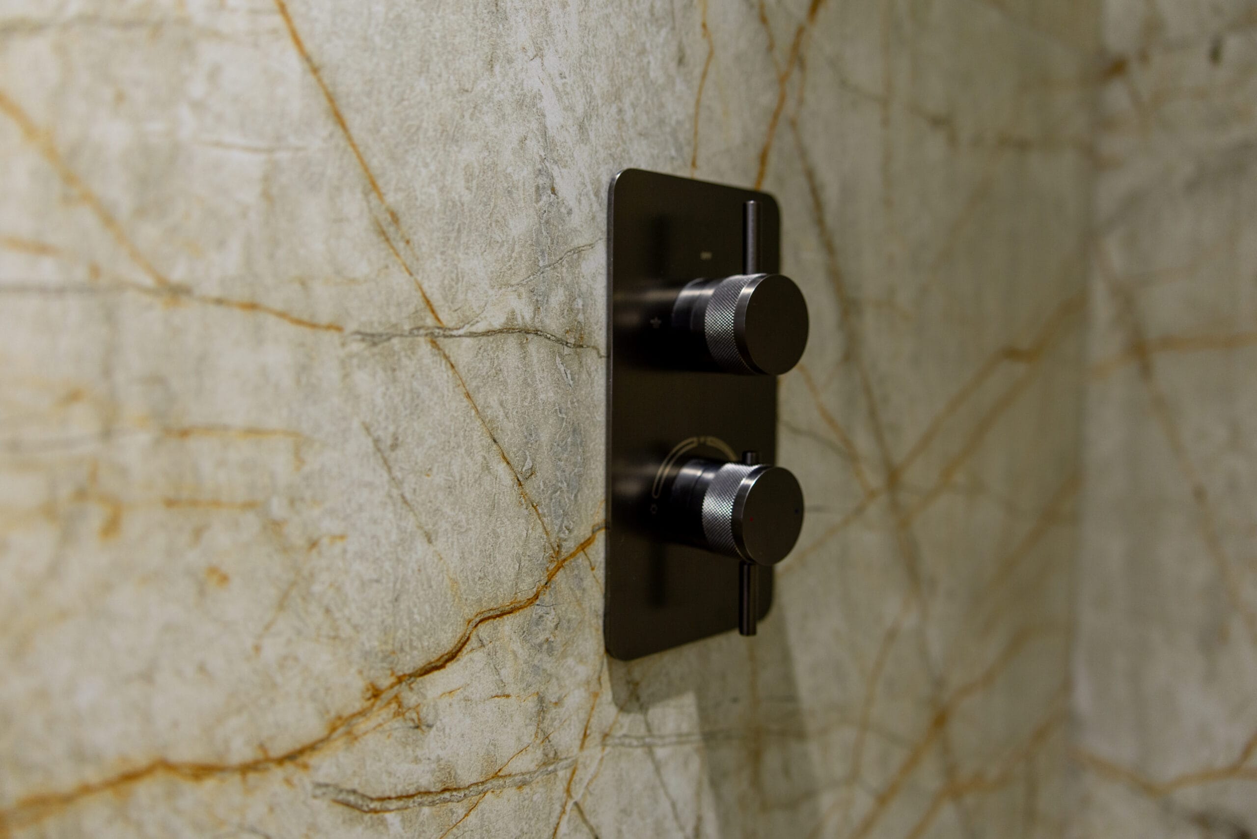Off white stone wall tiles with gold veins and black shower taps