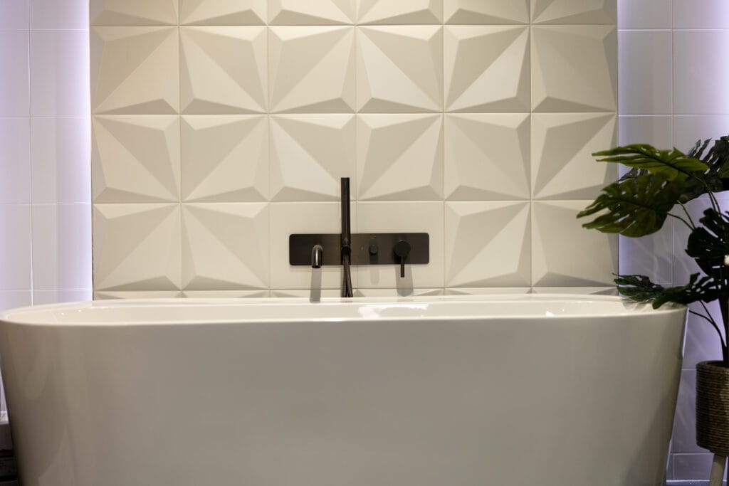 White 3D geometric wall tiles behind a freestanding bath with a matt black wall-mounted bath filler