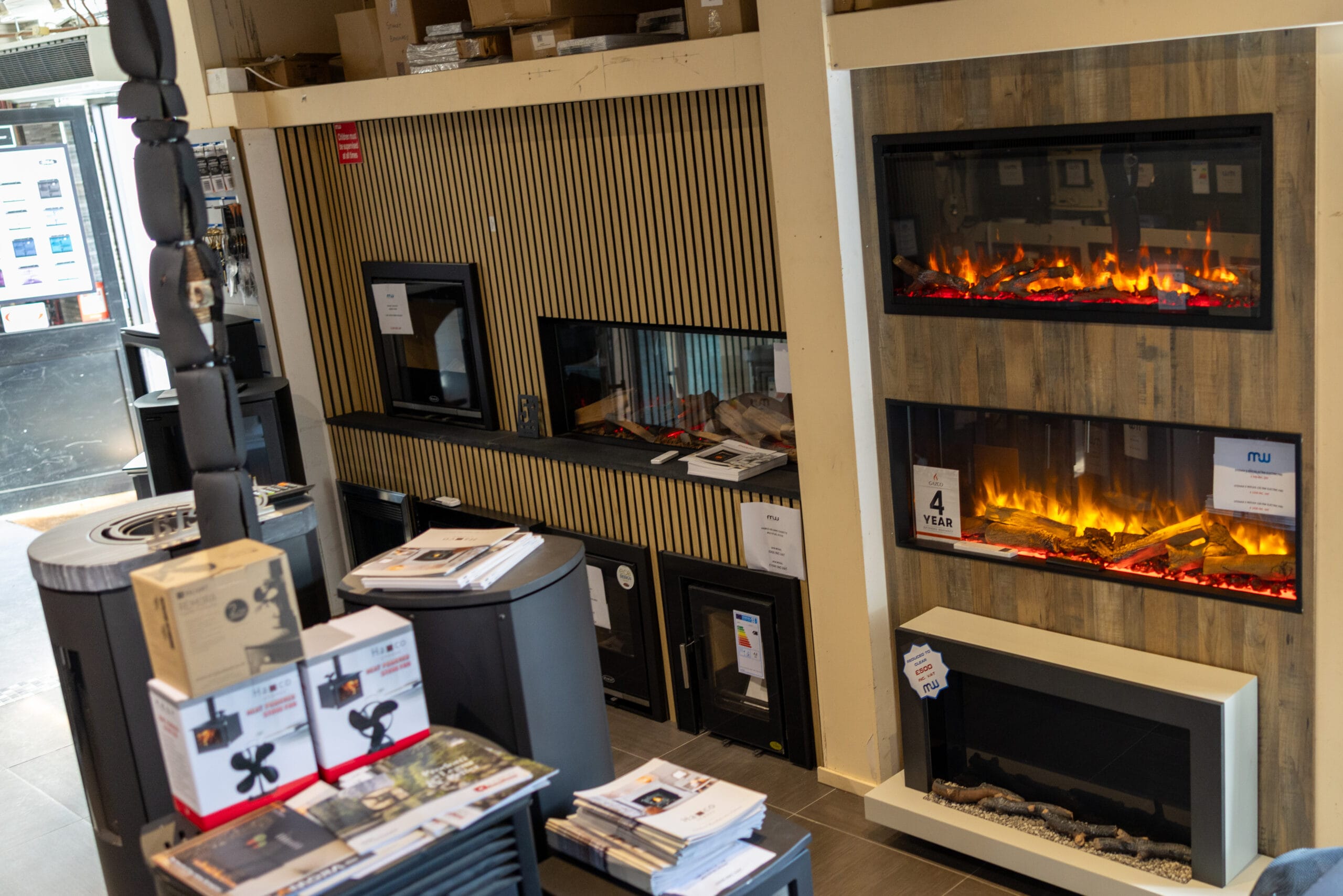 Electric fires with log-effect flames set into wood-panelled display walls, with stoves in the foreground of the Miller Wholesale stove showroom